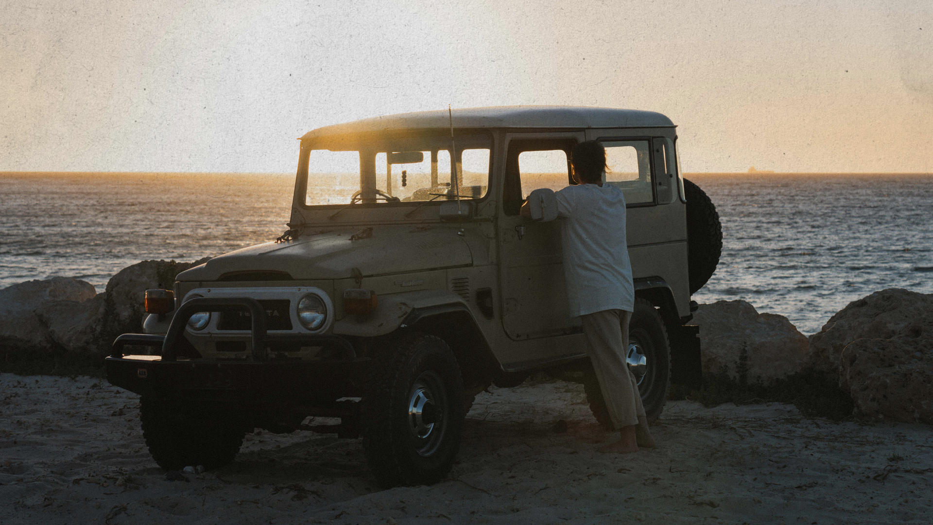 Sunset view of a man looking out to the ocean through his 4wd landcruiser and his reusable air freshener hanging from the rear view mirror 